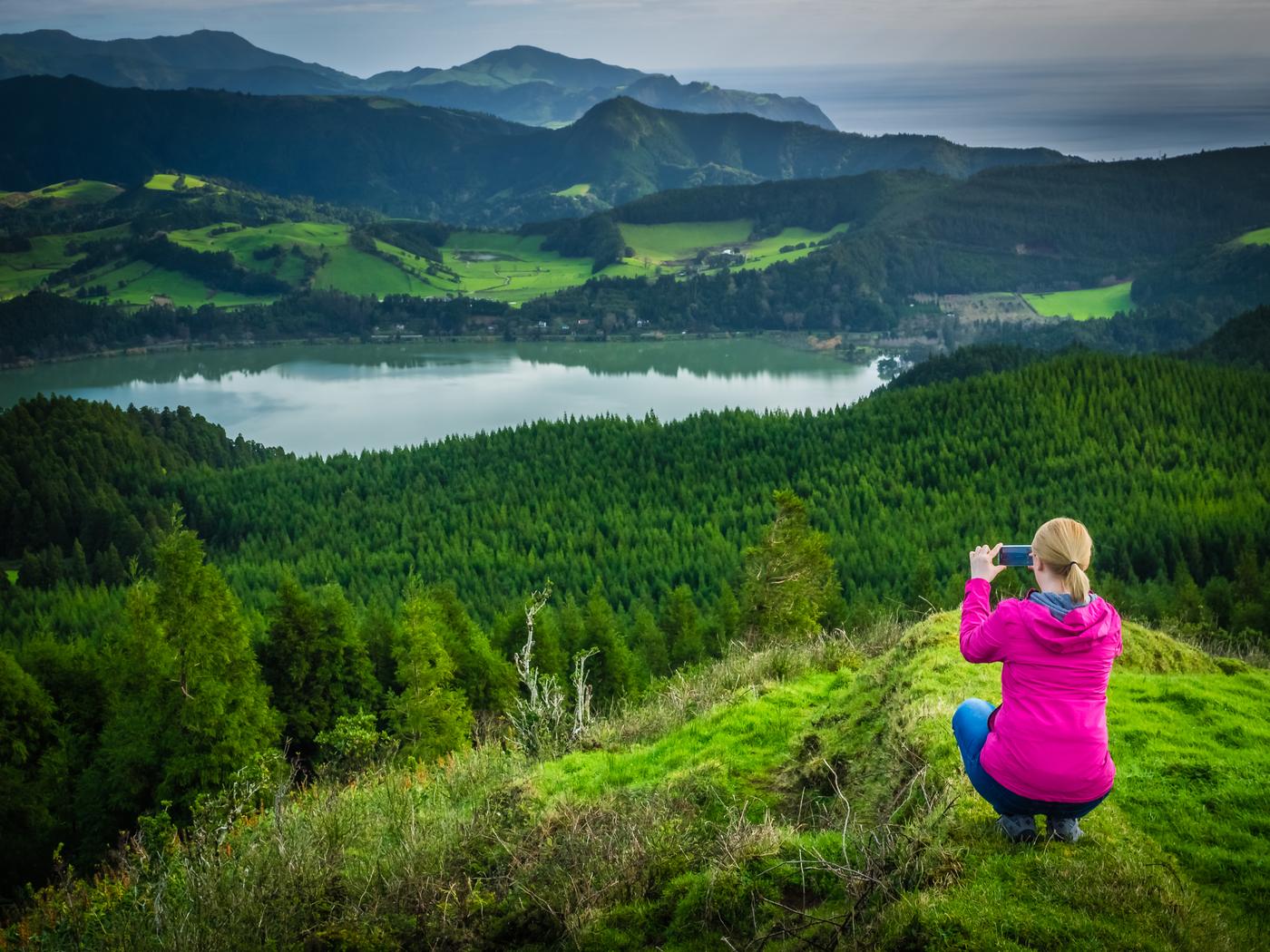 A traveller photographing a lake and green hills