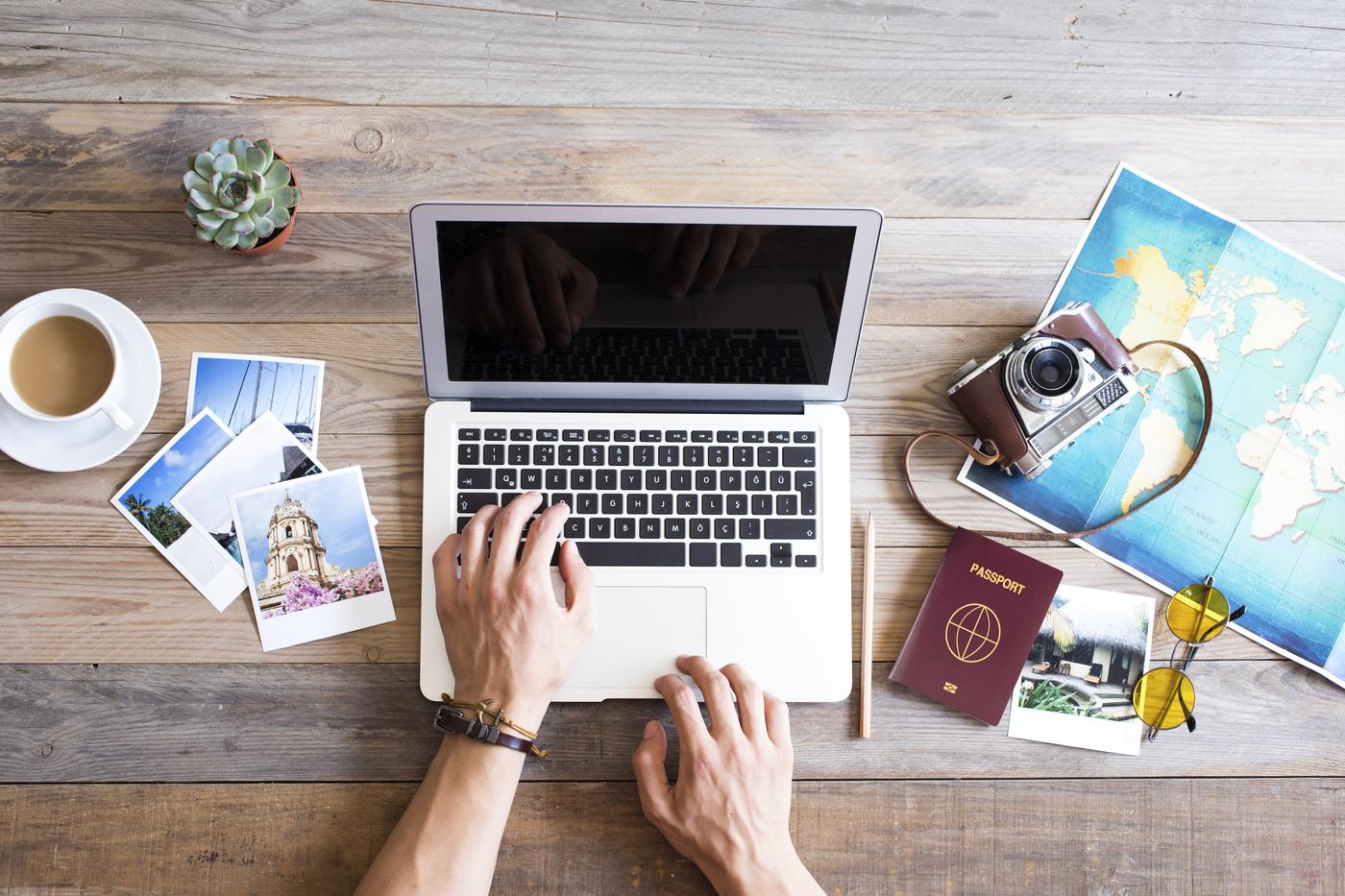 Hands on a laptop beside a map, passport and camera
